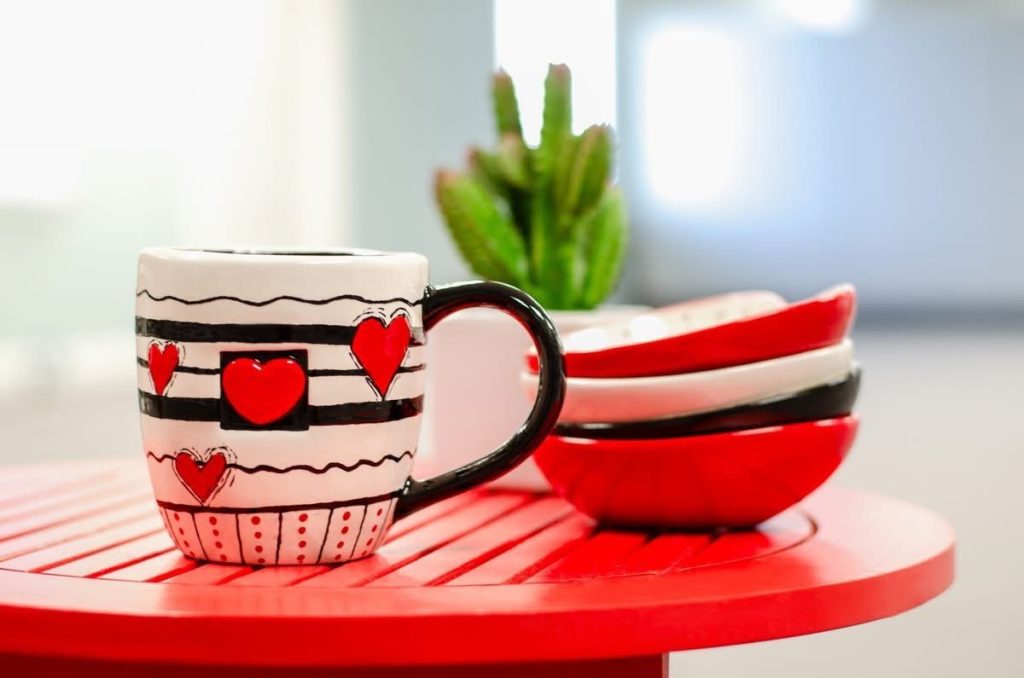 Hand-painted black, white, and red striped heart mug beside stacked red and black bowls