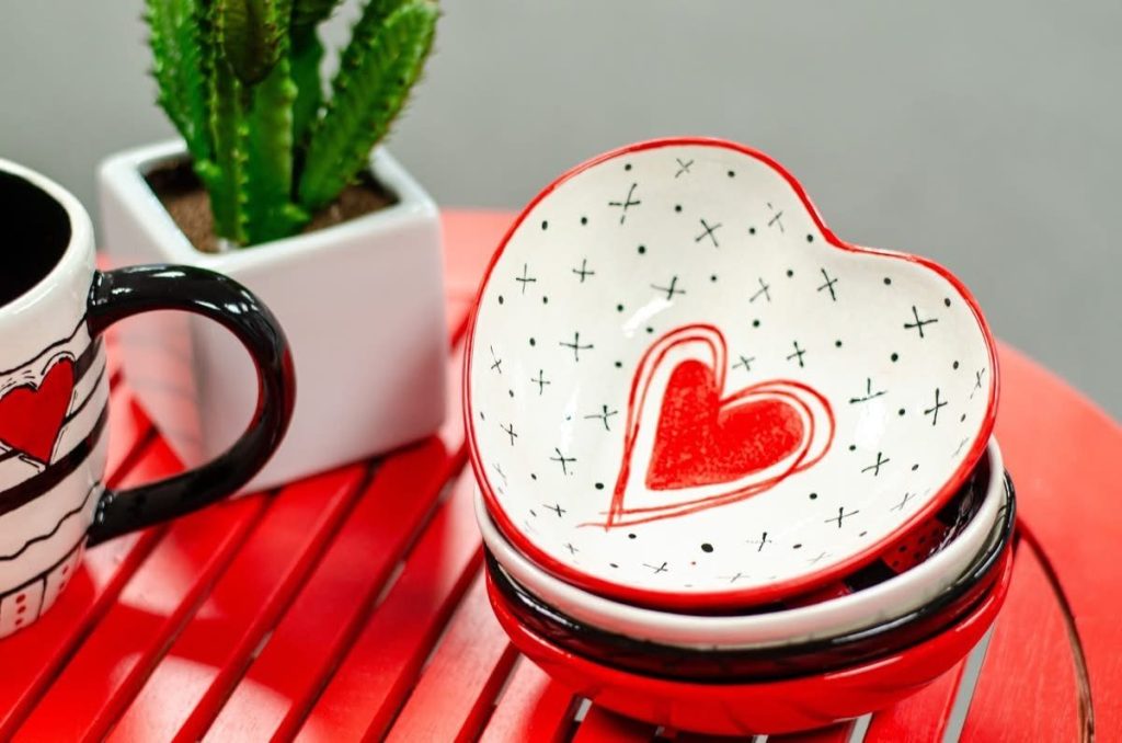 Hand-painted white heart bowl with a red outlined heart and black x pattern beside a striped mug