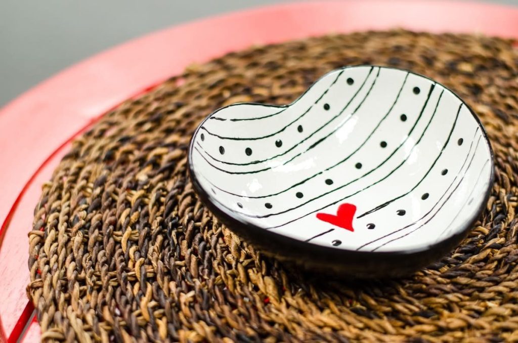 Hand-painted white heart-shaped bowl with black curved lines, dots, and a tiny red heart