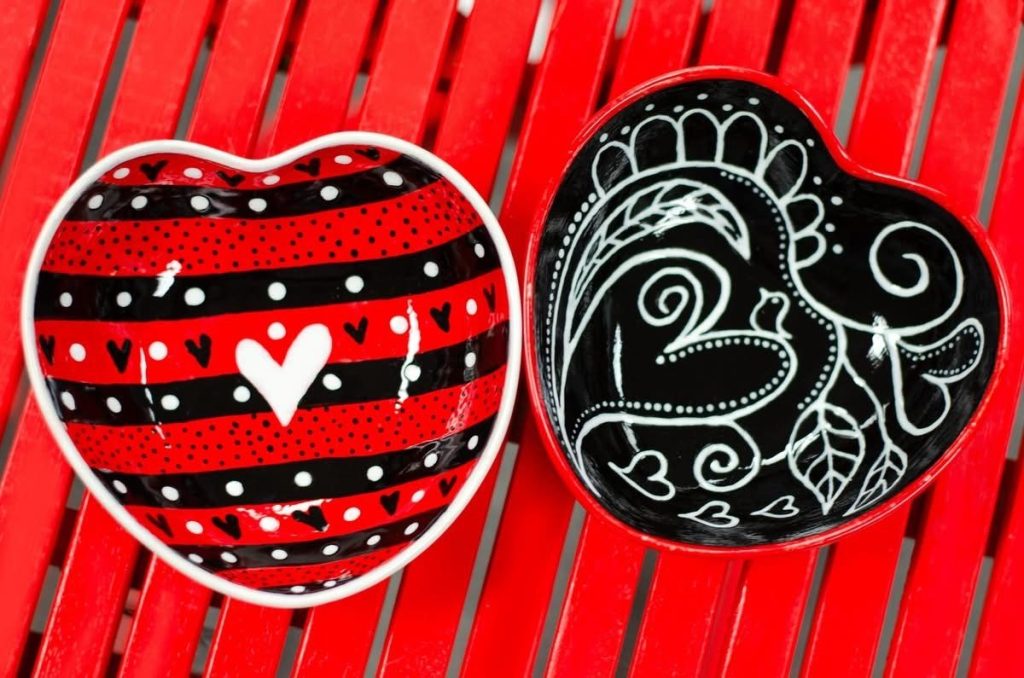 Two hand-painted heart bowls, one in red and black stripes and one with white paisley on black