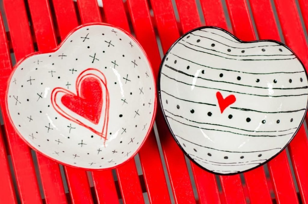 Two hand-painted white heart bowls, one with a red outlined heart and one with black curved stripes